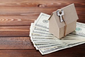 Model of cardboard home with key and dollar money. House building, insurance, housewarming, loan, real estate, cost of housing or buying a new home concept.