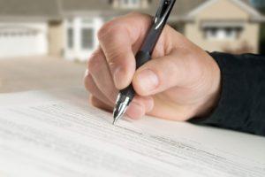 A hand holding a pen, writing on a financial document.
